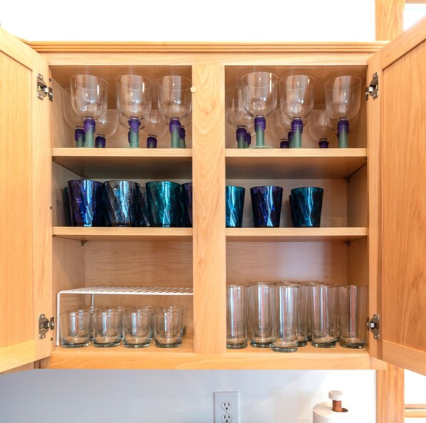 Un armario de madera con estantes que exhiben diferentes tipos de cristalería, incluyendo copas de vino, vasos y vasos para licor.