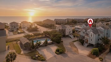 Un quartier résidentiel avec des maisons, une piscine et une vue sur l’océan au coucher du soleil.