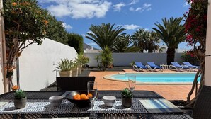 A patio with a table set for two, a pool, and lounge chairs in the background. - Beautiful Villa with a private heated pool and roof terrace. (Playa Blanca)