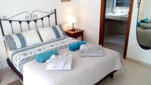 A neatly made bed with a patterned bedspread and pillows, a bedside lamp, and a view into a bathroom with a mirror and sink. - Beautiful Villa with a private heated pool and roof terrace. (Playa Blanca)