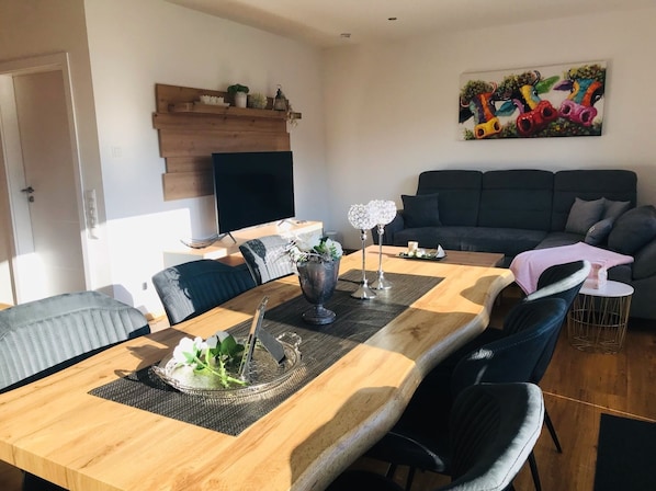 Un soggiorno moderno con zona pranzo, che include un tavolo da pranzo in legno, sedie nere, un divano nero e un quadro astratto dai colori vivaci appeso al muro.