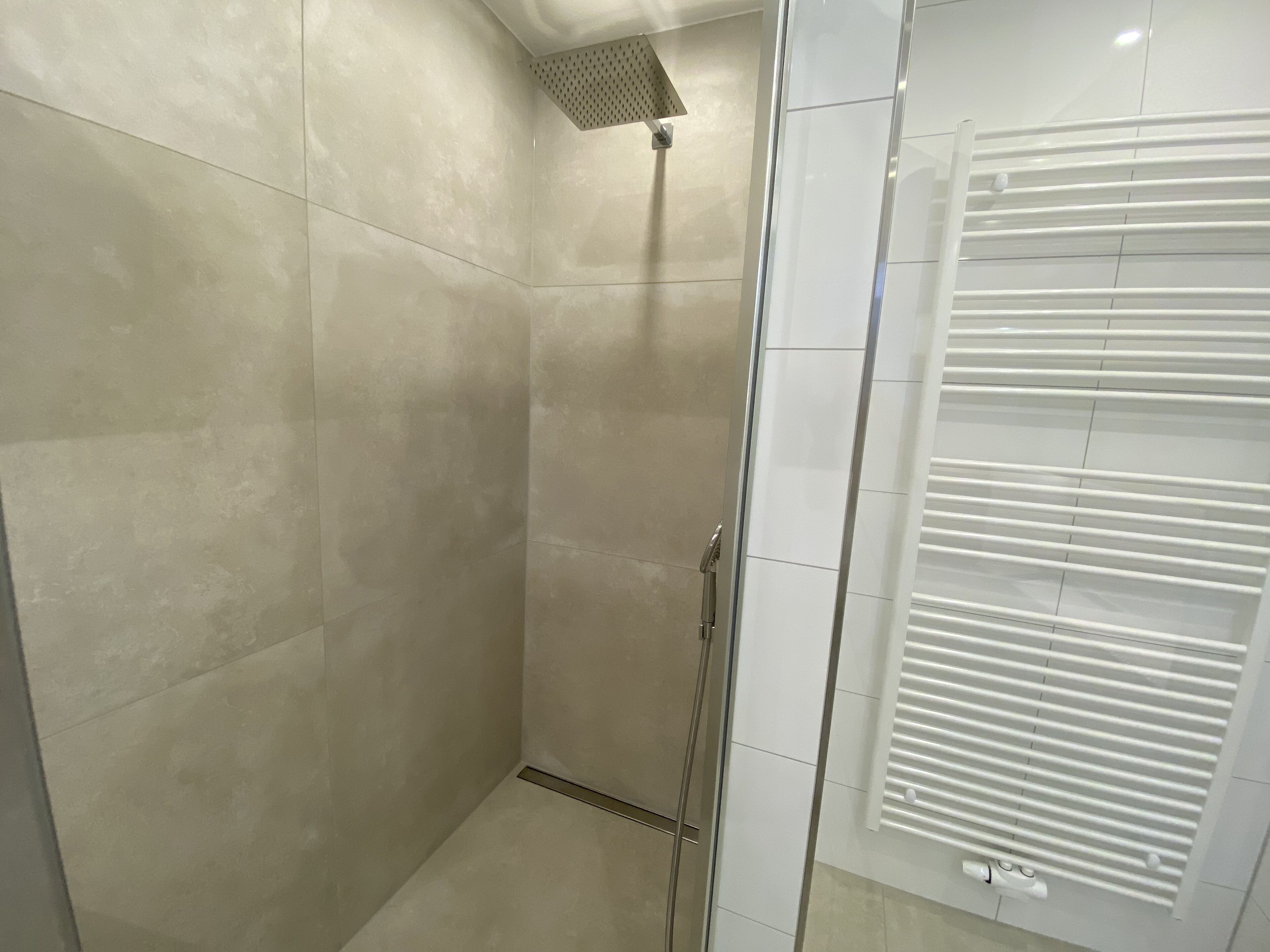 A modern bathroom with a glass shower enclosure, a white tiled wall, and a white radiator.