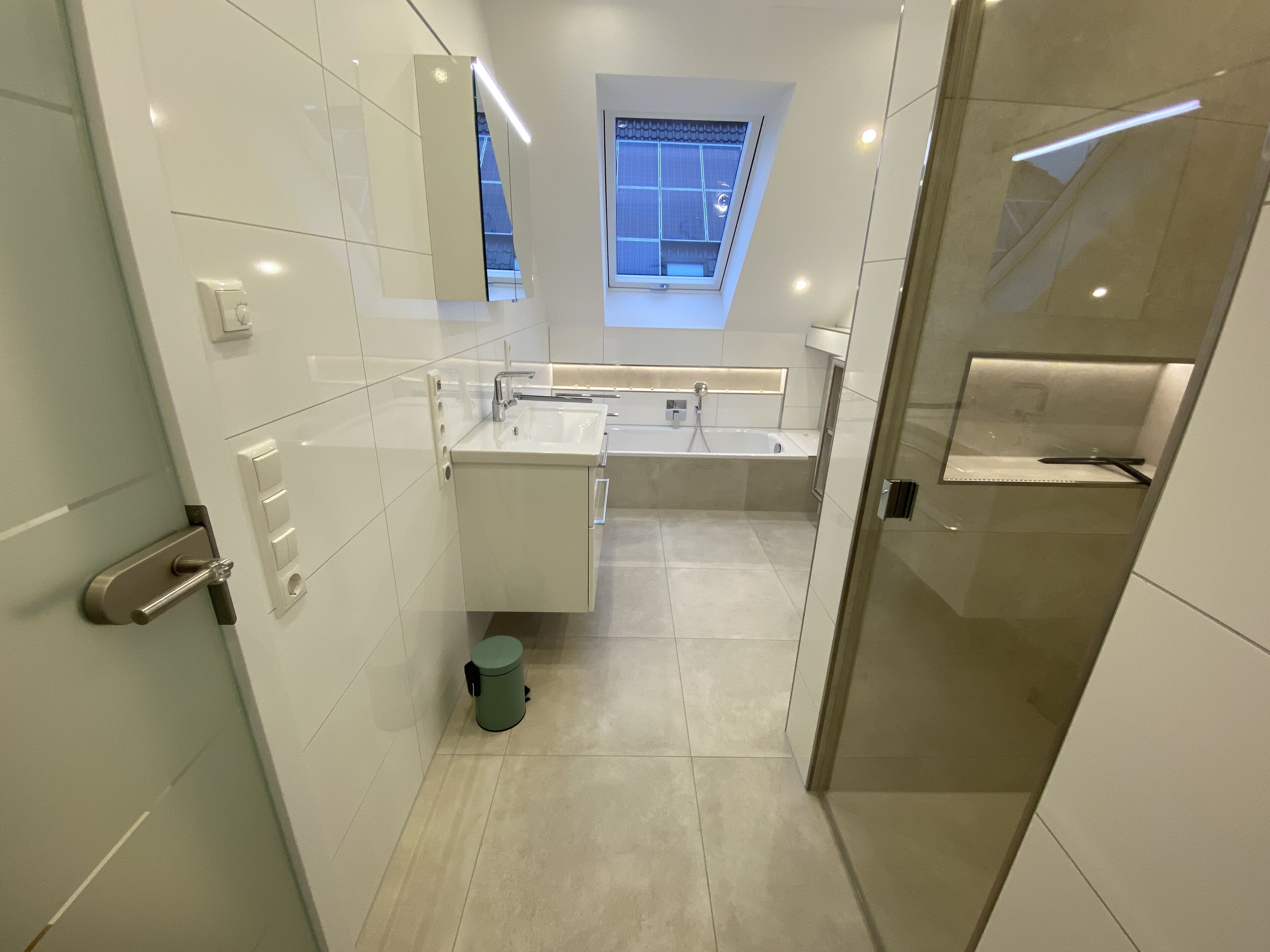 Een moderne badkamer met dakraam, grote spiegel en een ruime douche.