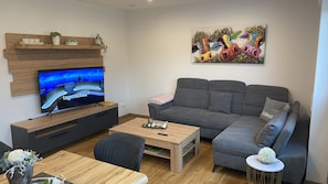 Un soggiorno moderno con una televisione a schermo piatto, un divano grigio, un tavolino in legno e un quadro con dei tori.