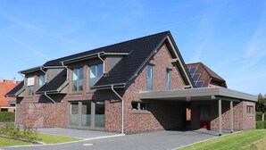 A modern two-story house with a brick exterior, large windows, and a covered driveway. - Relax in the luxury vacation home Geest & Moor 1 (Großheide)