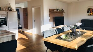 A modern kitchen with white cabinets, a built-in oven, and a dining area with a wooden table and black chairs. - Relax in the luxury vacation home Geest & Moor 1 (Großheide)
