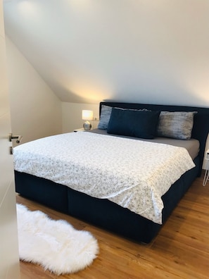 Una camera da letto con un letto, un comodino, una lampada e un tappeto bianco soffice.