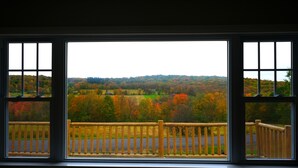 A view through a window with a wooden railing, overlooking a landscape with autumn-colored trees and a hilly background. - Mountain Getaway w/ Hottub, Views, Gamesroom, Fire Pit (Roxbury)