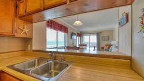 A kitchen with wooden cabinets, a stainless steel sink, and a view of a balcony with a chair and a table. - Sea Oaks 107, 2 Bedroom, 2 Bathroom, Oceanfront condo (Garden City Beach)