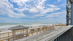 A beach view from a balcony with a wooden deck, a beach umbrella, and a pier in the distance. - Sea Oaks 107, 2 Bedroom, 2 Bathroom, Oceanfront condo (Garden City Beach)
