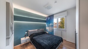 A modern bedroom with a bed, bedside table, and a view of the outdoors through a window. - Maisonnette Il Todeschino B12 by Wonderful Italy (Sirmione)