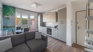 A modern kitchen with white cabinets, a built-in oven, and a dining area with a gray sofa and a small table. - Maisonnette Il Todeschino B12 by Wonderful Italy (Sirmione)