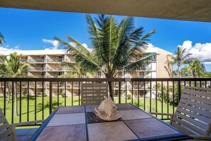 Un balcon avec une table et des chaises, donnant sur une piscine et des palmiers, avec un bâtiment en arrière-plan.