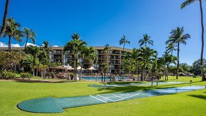 Um hotel com área de piscina, palmeiras e quadra de tênis.