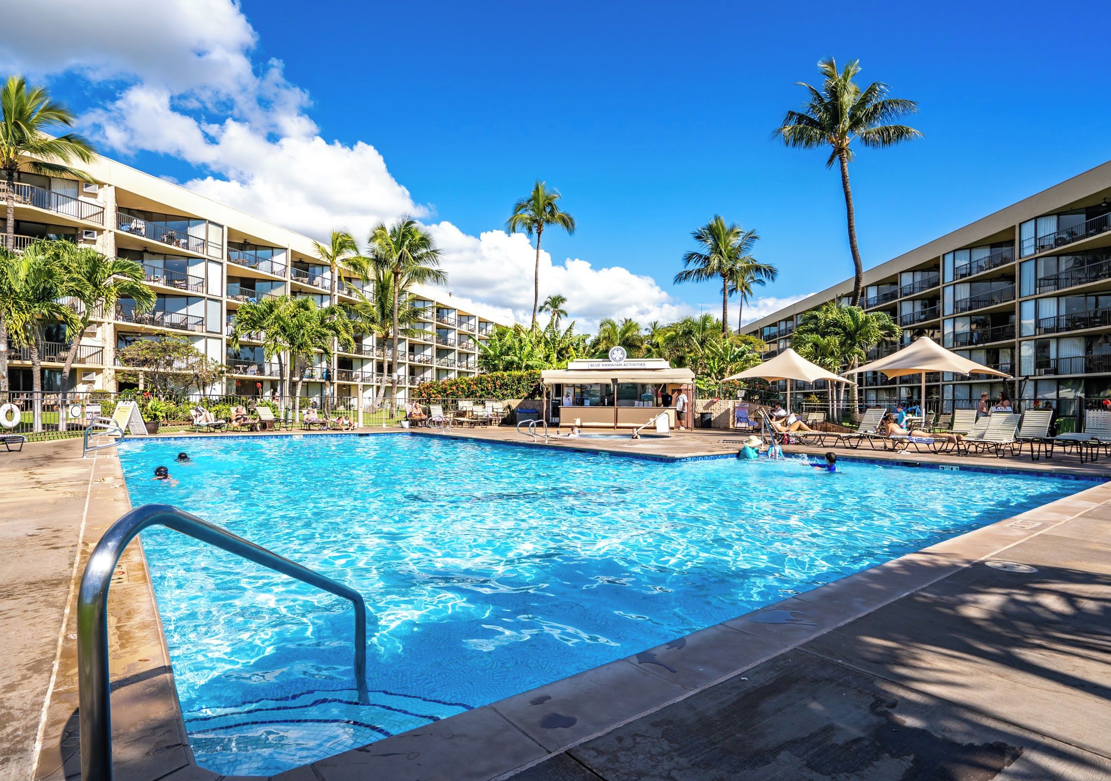 Ein Hotelpoolbereich mit mehreren Balkonebenen, Palmen und Liegestühlen.