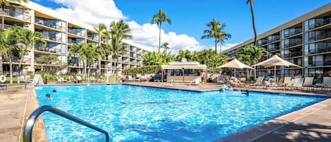 A hotel pool area with multiple levels of balconies, palm trees, and lounge chairs.