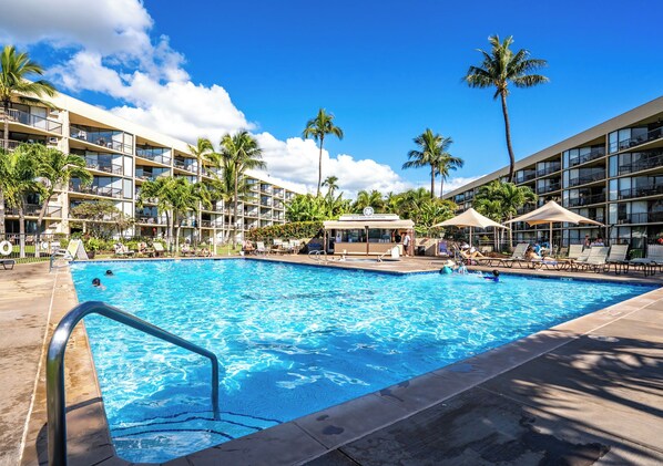 Un espace piscine d’hôtel doté de plusieurs niveaux de balcons, de palmiers et de chaises longues.