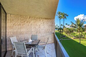 Un balcon avec une table et des chaises, un mur à la texture intéressante et une vue sur une pelouse bien entretenue et des palmiers.