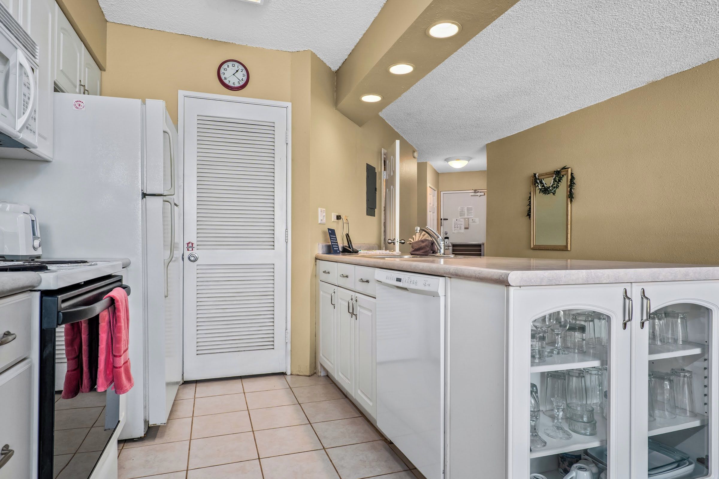 Una cocina con armarios blancos, un refrigerador blanco, un reloj en la pared y una puerta con ventana.