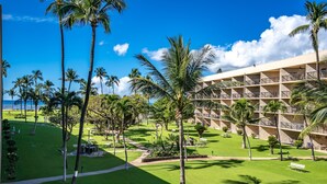 Um hotel com várias varandas, um gramado bem cuidado e palmeiras.