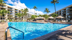 Área de piscina de hotel com vários níveis de varandas, palmeiras e espreguiçadeiras.