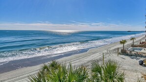 Strandudsigt med en træterrasse, en pool og en mol i baggrunden.