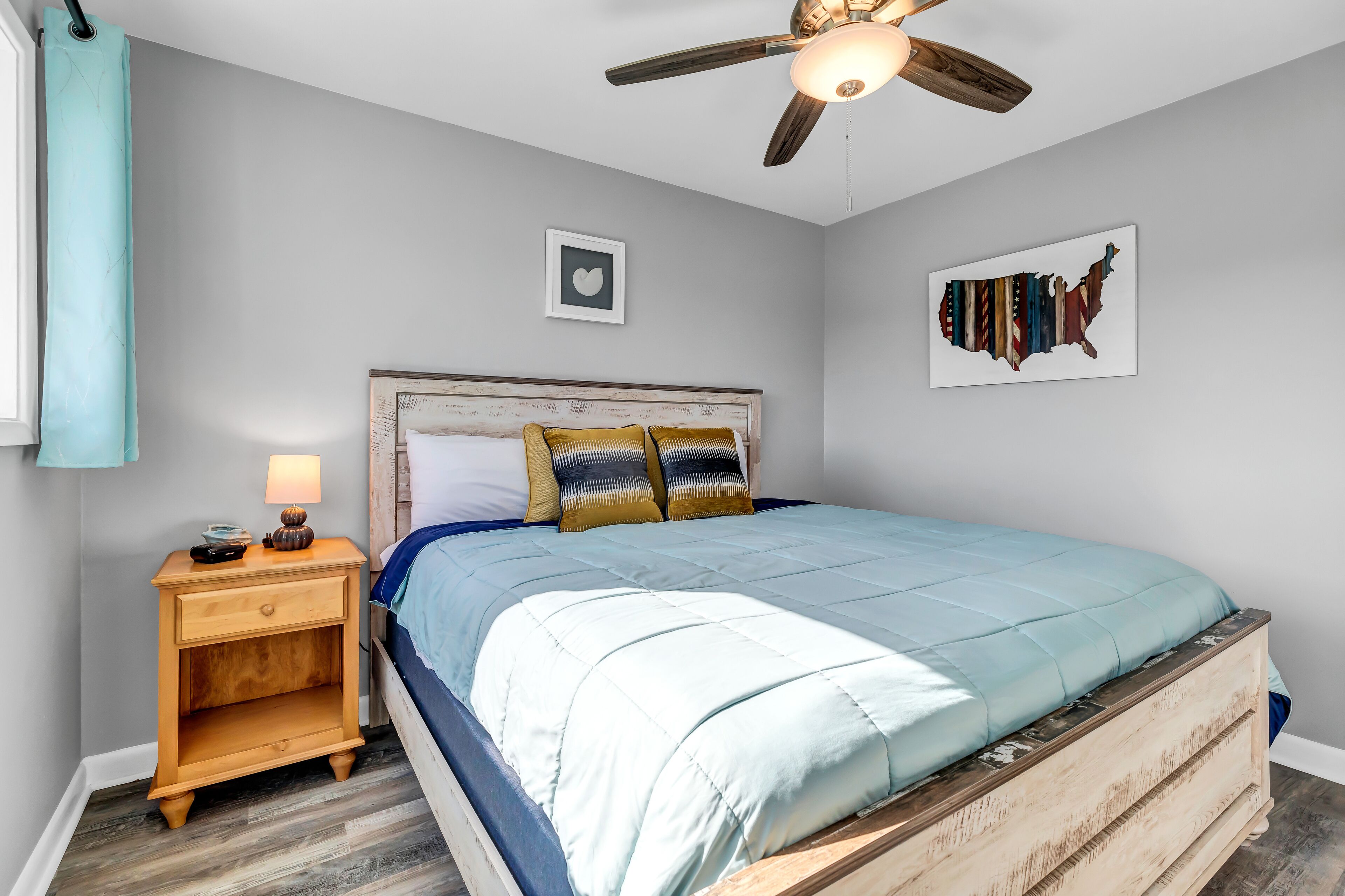 Une chambre à coucher avec un lit, une table de chevet en bois, un ventilateur de plafond et des œuvres d’art murales.