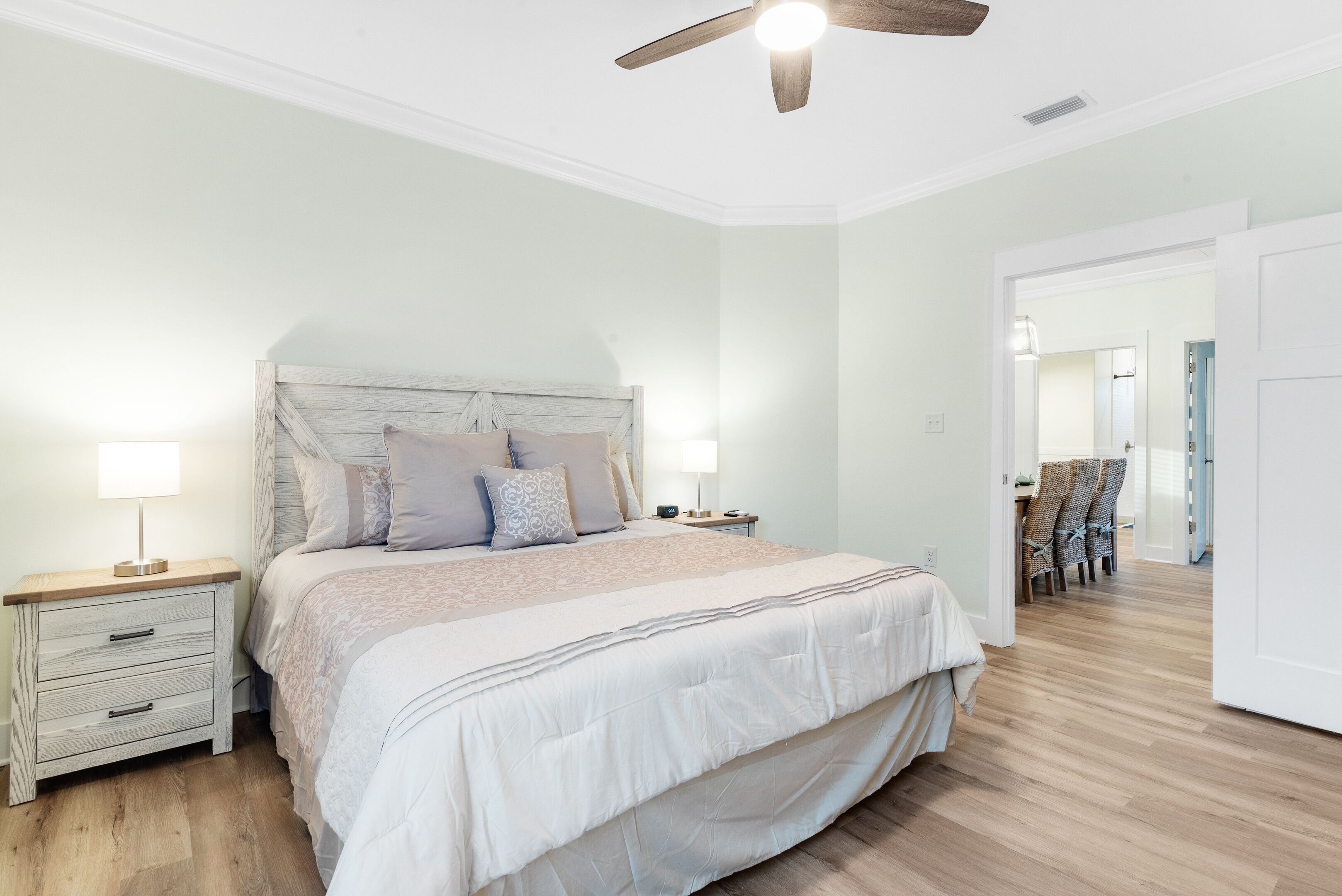 Un dormitorio con cama, mesitas de noche, ventilador de techo y vista a otra habitación.