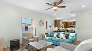 A living room with a sofa, armchairs, a coffee table, and a dining area with wooden cabinets and a microwave. - The Rookery III 7022 by RedAwning (Gulf Shores)