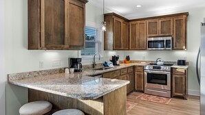 A kitchen with wooden cabinets, granite countertops, a stainless steel oven, and a built-in microwave. - The Rookery III 7022 by RedAwning (Gulf Shores)