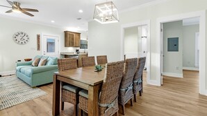A spacious living room with a wooden dining table, wicker chairs, a teal sofa, and a ceiling fan. - The Rookery III 7022 by RedAwning (Gulf Shores)