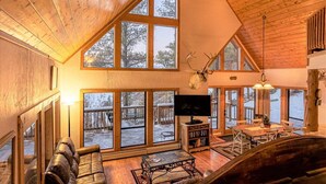 Un salón amplio con ventanas grandes, una chimenea, un televisor y una zona de estar acogedora.
