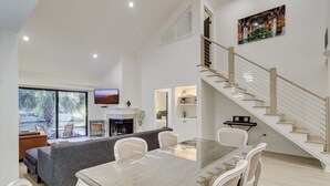 Ein modernes Wohnzimmer mit Essbereich, einer Treppe und einem großen Fenster.