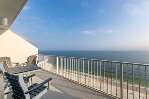 A balcony with a view of the sea, a white railing, and two Adirondack chairs.