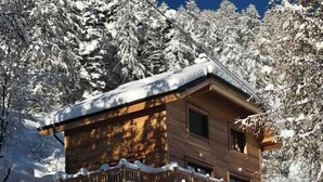 Een houten chalet met balkon, omringd door met sneeuw bedekte bomen.