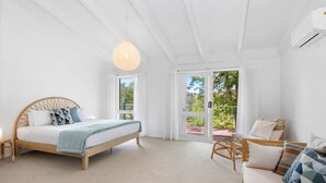 A bedroom with a bed, a sofa, a wicker chair, and a large window with a view of greenery. - Bellarine Lake House Ocean Grove (Ocean Grove)
