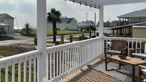Un espace extérieur abrité doté d’une terrasse en bois, d’une balustrade blanche, de guirlandes lumineuses et de mobilier d’extérieur.