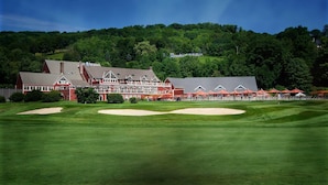 A golf course with a clubhouse featuring multiple buildings and a forested hill in the background. - Windfall @ Quechee Club VT: Cozy Updated Condo  A/C, Fireplace -Ski -Golf -Renew (Hartford)