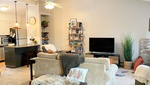 A modern living room with a sofa, a coffee table, a TV, and a kitchen area with a microwave and refrigerator. - Windfall @ Quechee Club VT: Cozy Updated Condo  A/C, Fireplace -Ski -Golf -Renew (Hartford)