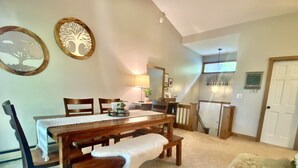 A dining area with a wooden table, chairs, and a bench. There are wall decorations, a lamp, and a staircase leading to another room. - Windfall @ Quechee Club VT: Cozy Updated Condo  A/C, Fireplace -Ski -Golf -Renew (Hartford)