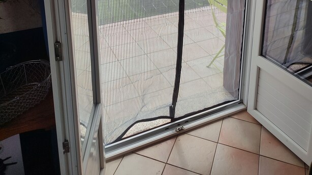 A sliding glass door with a mesh screen, leading to an outdoor area with a tiled floor and a view of a grassy field.
