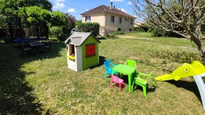 A house with a small playhouse and outdoor furniture in a grassy yard.
