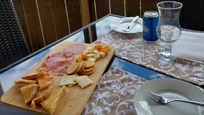 A table with a wooden board of assorted cheeses and meats, a can of beer, a glass, and a plate with a fork. - House with Stunning Ocean View (Mulgrave)