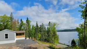 A cabin with a gravel driveway, a wooden deck, and a view of a lake. - House with Stunning Ocean View (Mulgrave)
