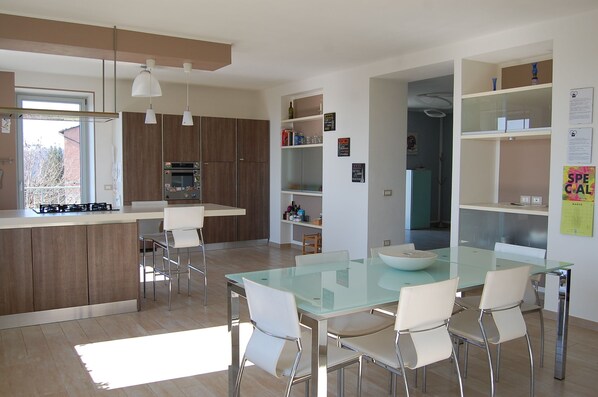 Una cocina moderna con una isla central, taburetes de bar y una mesa de comedor de cristal con sillas.