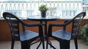 Ein runder Tisch mit zwei Stühlen, einem Blumentopf und Blick durch ein Fenster mit einem gestreiften Vorhang.