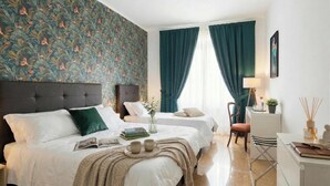 Ein Hotelzimmer mit zwei Betten, einem Schreibtisch, einem Stuhl, einer Lampe und einem fenster mit Vorhängen.