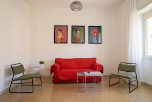 A room with a red sofa, two green chairs, a small table, and three framed artworks on the wall.