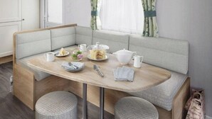 En matplats med ett träbord, bekväma sittbänkar och ett fönster med gardiner.
