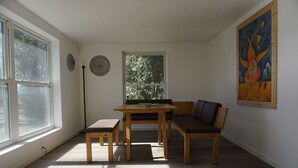 Una habitación con un ventanal grande, una mesa con sillas, un banco y un cuadro en la pared.